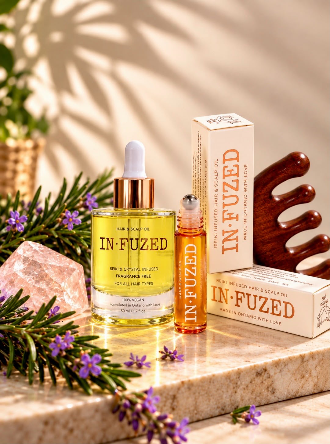 The IN·FUZED collection: Hair & Scalp Oil, roll-on, sandalwood comb and gift boxes on marble with rosemary and rose quartz