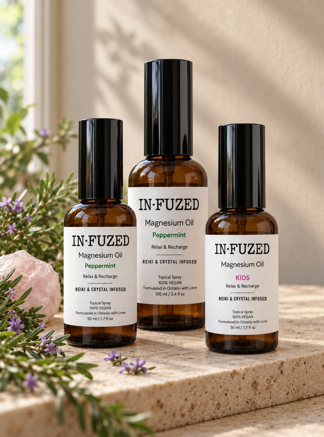 IN·FUZED Magnesium Oil trio: Peppermint 50 ml, Peppermint 100 ml and Kids 50 ml spray bottles in soft window light with rosemary and rose quartz
